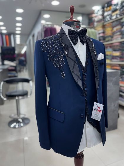 A striking navy blue three-piece tuxedo with asymmetrical black embroidery. The lapel features a unique diamond pattern, adding a geometric flair to the design.