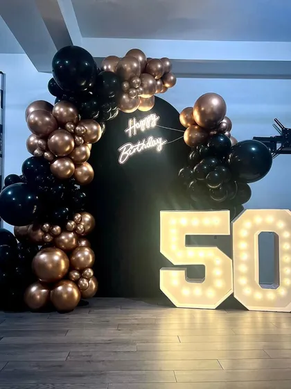 For milestone celebrations, like a 50th company anniversary, I provide impactful decor like these large, 4-foot marquee light-up numbers. Paired with a custom neon sign and a sophisticated black and bronze balloon arch, it creates a perfect photo backdrop.
