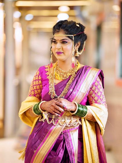 A classic Maharashtrian bridal look with a purple and yellow Paithani saree. The bride is adorned with a Mundavalya, nath, and traditional gold jewellery.