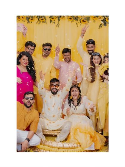 A fantastic group photo with the couple and their friends during the Haldi. It’s a moment of shared celebration, with flower petals flying and everyone dressed in vibrant yellows.