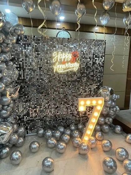 A glamorous 7th-anniversary celebration featuring a floor-to-ceiling silver sequin backdrop, a neon sign, and a large illuminated number '7'.