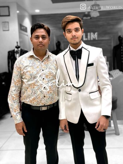 The designer with a client, who is wearing a classic white tuxedo with black trim. This is a sharp, high-contrast look perfect for a formal party.