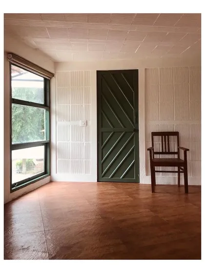 An interior view of a private farmhouse project, showcasing a minimalist aesthetic. The space is defined by its clean lines, an earthy oxide floor, and a large window that fills the room with natural light, creating a serene connection with the outdoors.