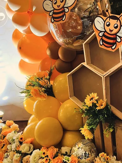 For our "Sweet as Honey" theme, we created this fun decor element using honeycomb shelves and cute bee cutouts. The setup is surrounded by yellow and orange balloons and florals, tying the whole look together.