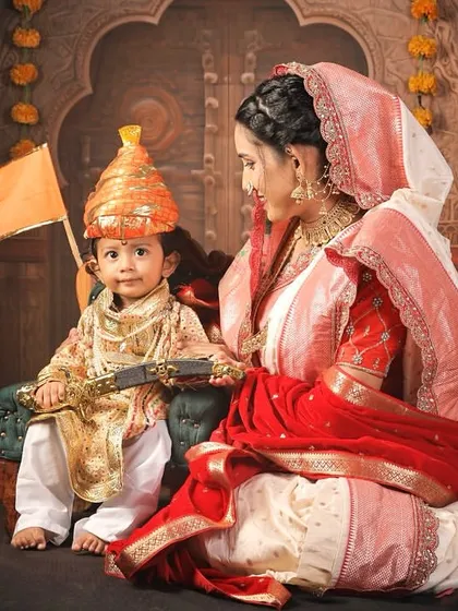 A regal portrait of "Jijamata" looking lovingly at her "Baal Shivaji," who holds the saffron flag, set against a backdrop resembling a Maratha court.