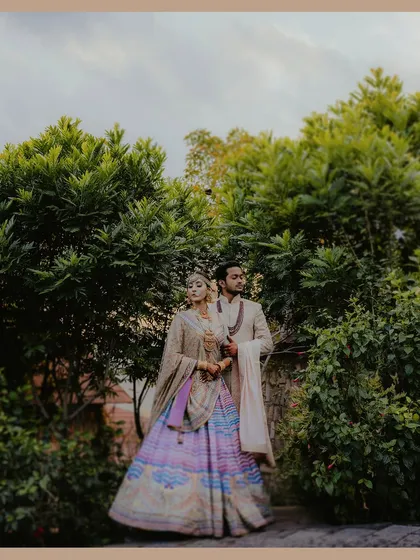 A stylish couple portrait set amidst lush greenery. The bride's unique multi-colored lehenga and the groom's classic sherwani create a visually stunning image.