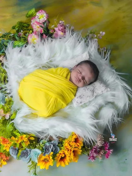 A newborn wrapped in yellow, nestled in a nest of white fur and surrounded by flowers. This creates a bright and happy portrait.