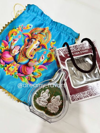 A lovely Ganpati return gift set, featuring a silver-plated Lakshmi and Ganesh frame inside a clear case, presented with a bright blue satin potli bag.