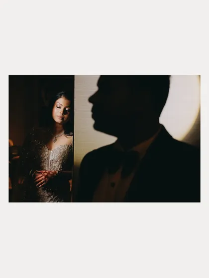 An artistic and moody couple portrait. The silhouette of the groom in the foreground creates depth and mystery, drawing the viewer's eye to the bride's serene expression.