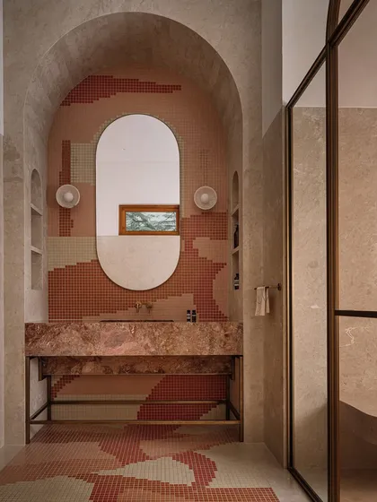 This bathroom is all about playful geometry, with pixelated mosaic tiles in earthy tones creating a dynamic pattern on the floor and walls. The design is anchored by a sculptural pink marble vanity, creating a space that is bold and full of personality.