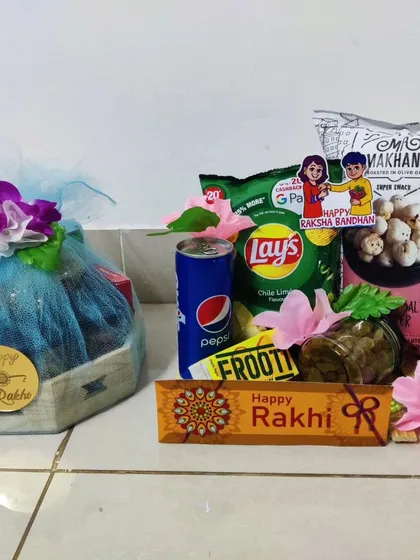 This is a great example of a simple and budget-friendly Rakhi gift. It includes a mix of popular snacks like Lays and makhana, a Pepsi can, and a Happy Rakhi chocolate bar, all neatly arranged for a thoughtful gesture.