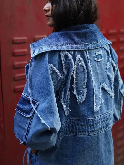 A detailed shot of the distressed denim jacket from Jaywalking, worn by Srishti Shrivastava. The frayed lettering on the back adds a custom, DIY feel to the grunge aesthetic.