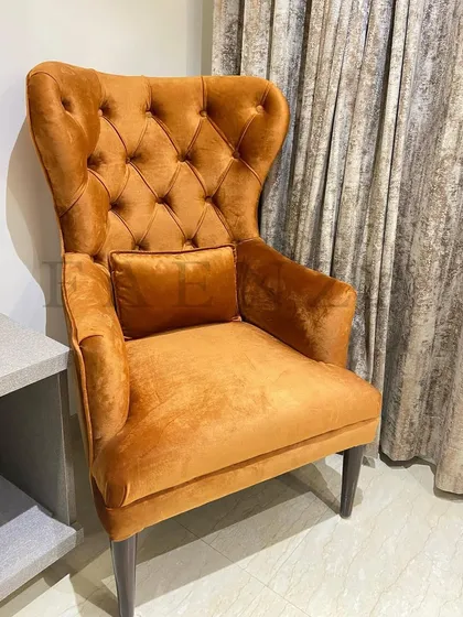 A classic wingback chair in a rich, mustard-colored velvet. The deep button-tufting and timeless shape make it a piece that adds warmth and sophistication to any room.
