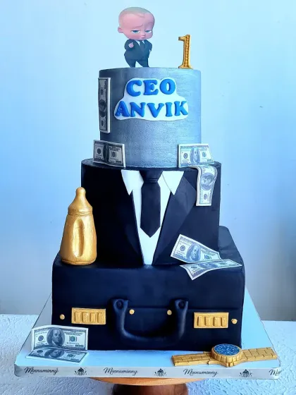 A detailed look at the three-tiered Boss Baby cake. It features a briefcase tier, a suit and tie tier, and a top tier with edible money and a "CEO" title.
