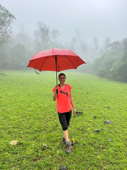 A trekker with a bright red umbrella walking through a lush green meadow on a foggy day. A beautiful, colourful contrast.