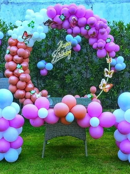 This vibrant outdoor birthday setup in a garden is perfect for a fun and colorful party. The balloon ring in shades of pink and orange, along with matching balloon pillars, creates a cheerful and inviting atmosphere.