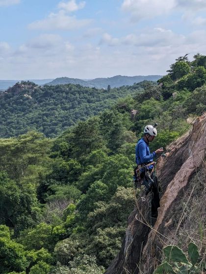 A climber at a belay station on a new route at Hosadurga, overlooking the green valley.