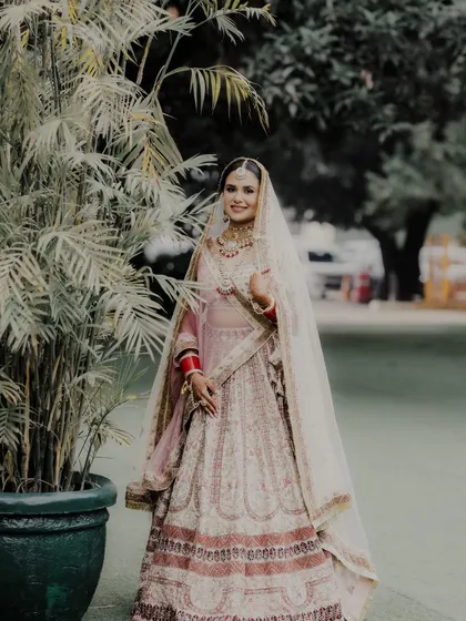 A full-length portrait of the bride, Shreya, in her beautiful pastel lehenga at Mallu Farms. She stands with grace and poise, ready for her big day.