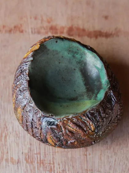 This small, textured bowl has a beautiful green interior that contrasts with the earthy exterior. It's a perfect example of functional art.