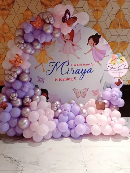 A magical fairy and butterfly theme for a 5th birthday, featuring a custom backdrop and a pastel purple and pink balloon garland.