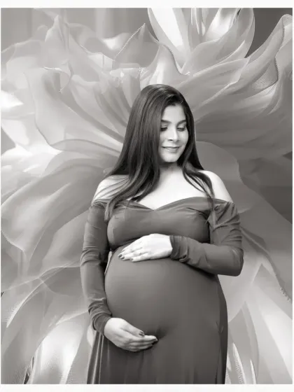 A serene black and white solo portrait of a mother-to-be cradling her bump, set against a soft, abstract floral background.