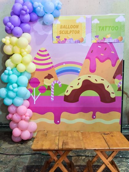 A "Balloon Sculptor" and "Tattoo" station set against a whimsical candy-mountain backdrop.