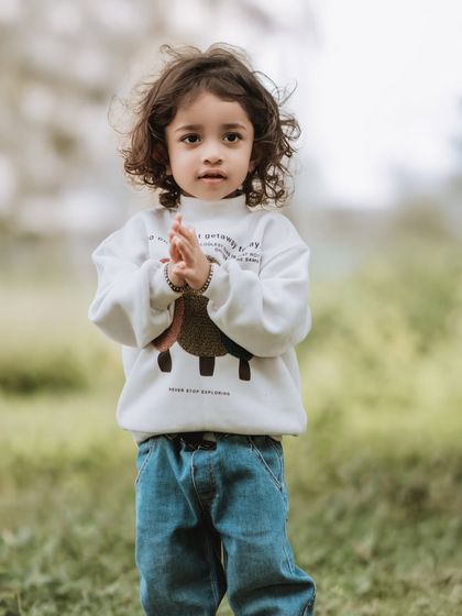 A full-length portrait of a little boy in a cute sweater, taken outdoors.