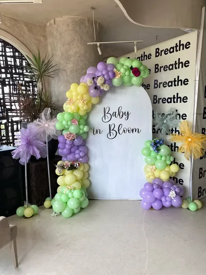 A 'Baby in Bloom' themed baby shower with a fresh pastel color palette. The decor features a personalized arched backdrop and a balloon garland in shades of lavender, yellow, and light green.