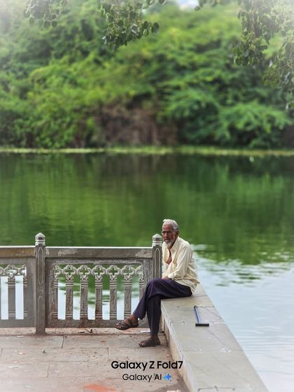 A quiet, environmental portrait of an elderly man sitting by the water. This shot captures a moment of peace and contemplation, blending the person with the serene landscape.