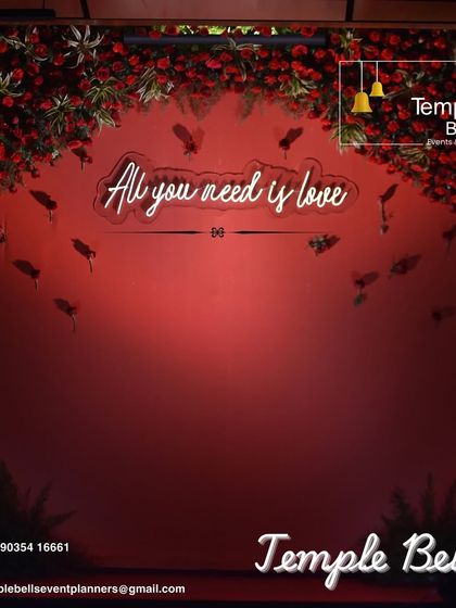 A romantic photo backdrop featuring a neon sign that reads "All you need is love". This simple yet impactful element, combined with a red floral frame, creates a perfect spot for couple and guest photos.