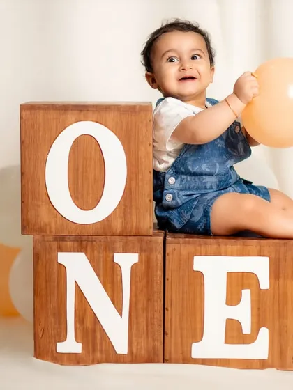 A happy baby boy celebrates turning one, sitting atop wooden blocks that spell out his big milestone. This classic studio setup is perfect for timeless first birthday portraits.
