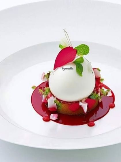A delicate and elegant dessert creation. A white chocolate sphere encloses a surprise filling, served on a bed of fresh berries and mint with a vibrant raspberry coulis.