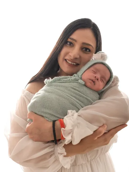 A new mother holds her swaddled baby close, smiling at the camera. The joy of new parenthood is so wonderful to capture.