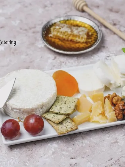 An elegant display of fine cheeses, perfect for an intimate gathering. This platter features a wheel of soft Brie, piquant blue cheese, and goat cheese, beautifully paired with crackers, grapes, dried apricots, walnuts, and a dish of pure honeycomb.
