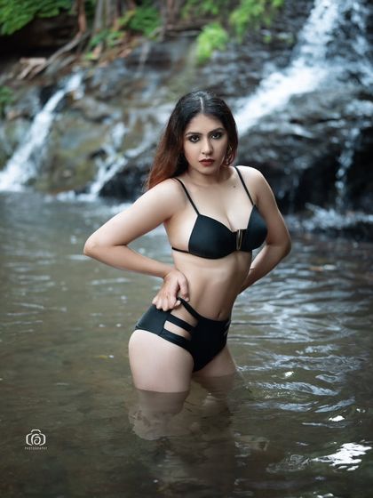 A powerful pose in a black bikini, standing in the cool water of a natural pool. The waterfall in the background adds a sense of drama and movement to the shot.