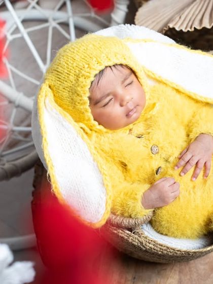 A newborn bunny sleeping in a basket, looking cozy and cute in a fluffy yellow costume.