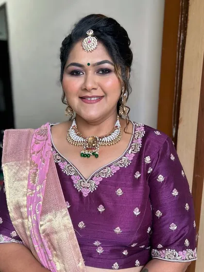 A traditional look with a modern twist. The makeup is classic, with a defined eye and a maang tikka, while the hair is styled in an elegant updo.