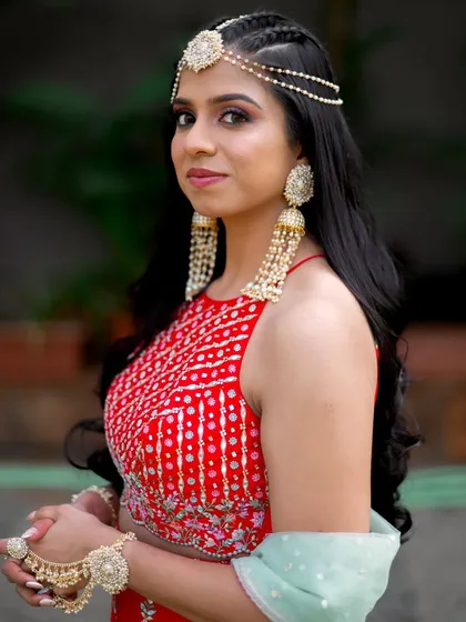A portrait of the bride ready for her Mehendi ceremony, looking stunning in a red outfit and statement jewelry.