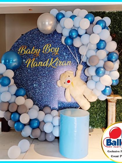A "Welcome Baby" party with a teddy bear theme. The setup features a blue, grey, and white balloon arch around a sparkling backdrop with a teddy bear floating with balloons.