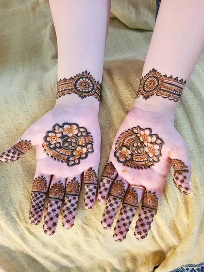 A lovely and dainty Eid henna design. The palms feature a small floral and paisley motif, with a delicate grid pattern on the fingers.