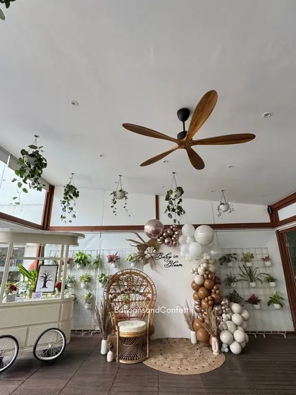 The full view of the baby shower setup in a beautiful, light-filled room. The hanging plants and greenery wall add to the 'in bloom' theme.