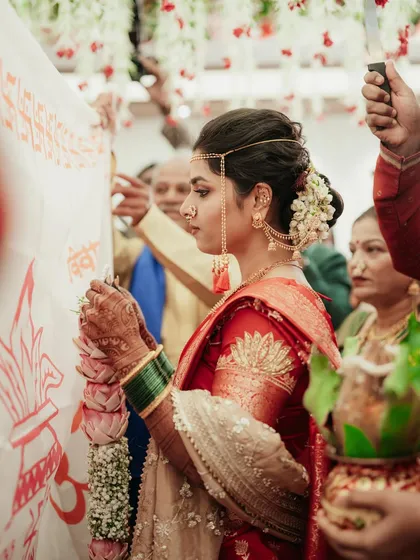 A candid moment from a wedding ceremony. The bride, in her red saree and traditional headwear, looks serene and beautiful.
