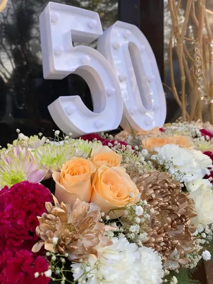 A close-up of the 50th birthday centerpiece. I used a mix of peach roses, red carnations, and white and gold chrysanthemums for a warm and celebratory color palette.