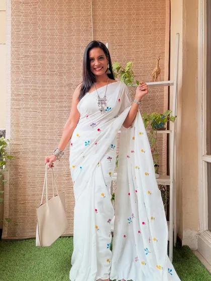 A white Khadi cotton saree with small, colorful embroidered motifs. It's a simple, elegant, and comfortable saree for daily wear.