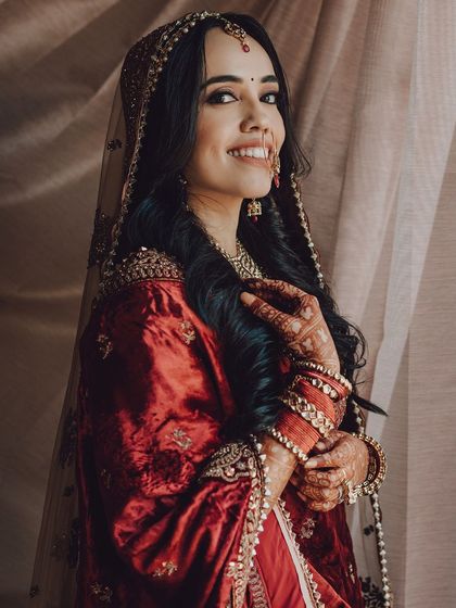 A warm, smiling portrait of the bride, her hands gently clasped, showcasing her henna and bangles.