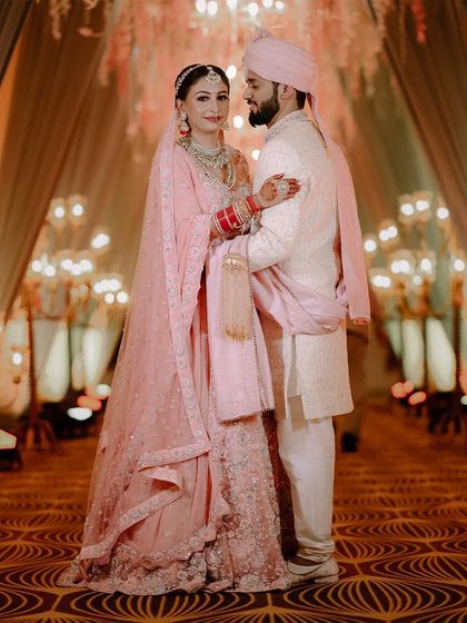 A full-length portrait of the couple at their Jammu wedding. The grand entranceway and their elegant pastel outfits create a beautiful, harmonious picture.