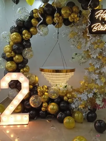 A luxurious black and gold theme for a 22nd birthday. The balloon arch is accented with white flowers and a hanging chandelier centerpiece, creating a very glamorous photo spot.