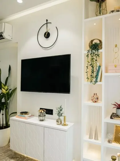 This bright and airy living area features a clean white TV unit and open shelving for displaying decor. The large plant adds a refreshing touch of nature, making the space feel vibrant and alive.