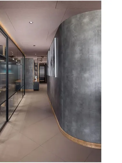 A curved, textured concrete wall defines the main corridor in the Paras Healthcare office, guiding movement through the space. This minimalist approach maximizes the potential of raw materials for a refined aesthetic.