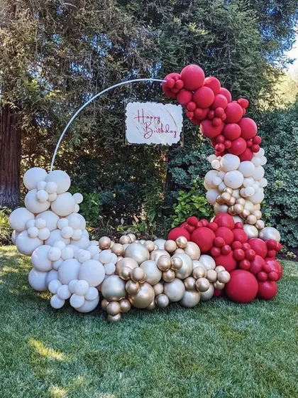 An elegant circular balloon arrangement for a garden party. The red, white, and gold balloons create a beautiful contrast with the natural green background.